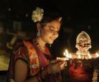 Mulher ajoelhada com uma lâmpada de azeite na mão na festa de Diwali