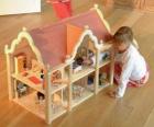 Garota brincando com uma boneca e uma casa de bonecas com mobília