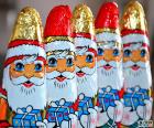 Cinco figuras do Papai Noel de chocolate, todos com um presente nas mãos