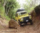 Um belo Land Rover Defender amarelo dirigindo em uma estrada